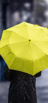 A person holding a yellow umbrella as they walk down a street